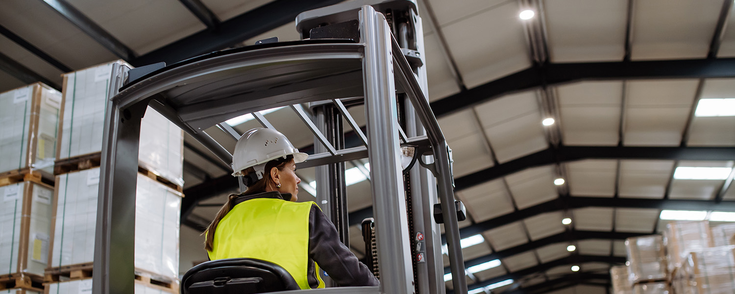 Interior warehouse shot of woman on forklift and roof lighting